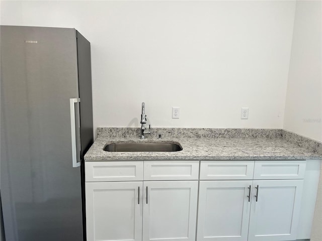 kitchen with stainless steel refrigerator, white cabinetry, sink, and light stone countertops