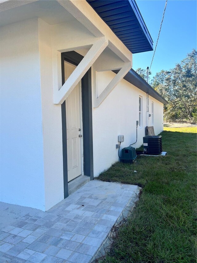 view of exterior entry featuring a lawn and central air condition unit