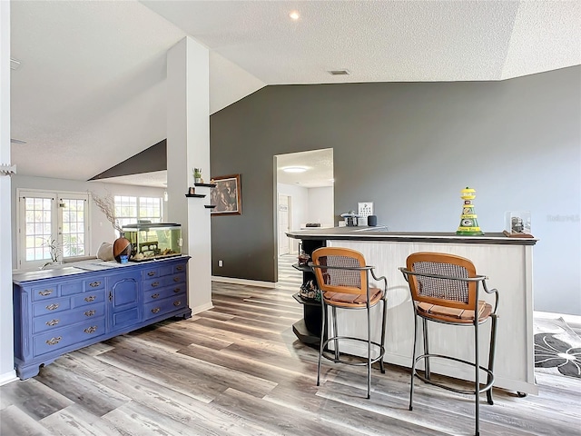 bar featuring a textured ceiling, light wood-type flooring, blue cabinets, and lofted ceiling