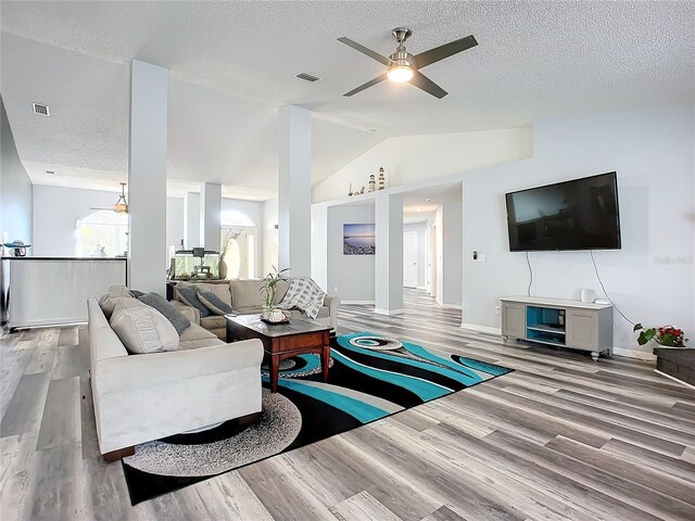 living room with a textured ceiling, ceiling fan, light hardwood / wood-style flooring, and lofted ceiling