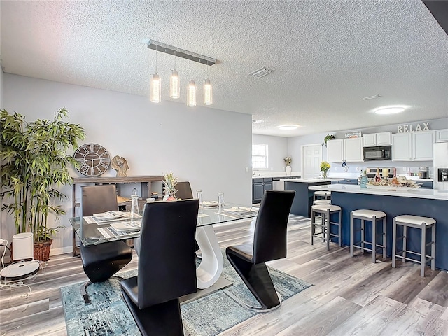 dining area with a notable chandelier, a textured ceiling, and light wood-type flooring