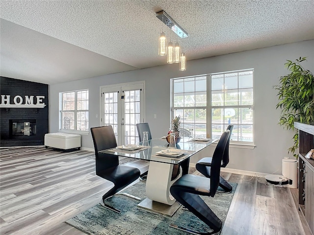 dining space featuring a wealth of natural light, light hardwood / wood-style flooring, a textured ceiling, and a brick fireplace