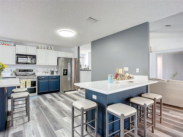 kitchen with a kitchen bar, white cabinetry, light hardwood / wood-style floors, and appliances with stainless steel finishes