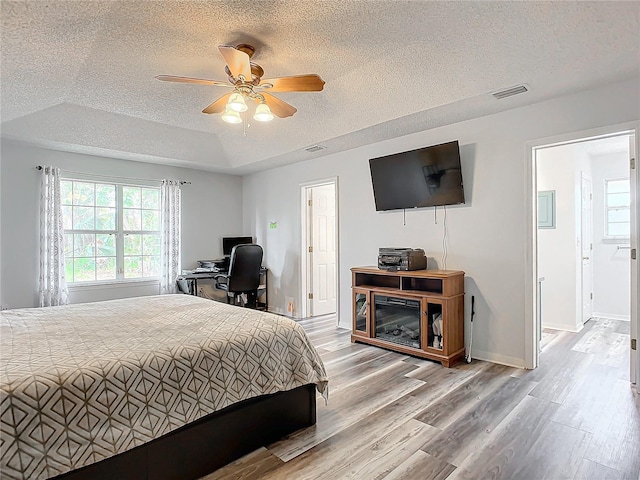 bedroom with a textured ceiling, hardwood / wood-style flooring, a raised ceiling, and ceiling fan