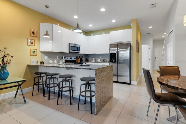 kitchen featuring white cabinetry, hanging light fixtures, stainless steel appliances, kitchen peninsula, and dark stone countertops