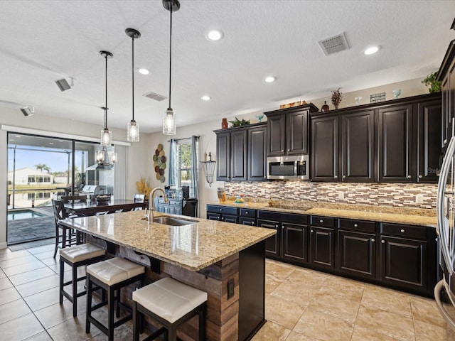 kitchen featuring sink, decorative light fixtures, a kitchen breakfast bar, light stone countertops, and a kitchen island with sink