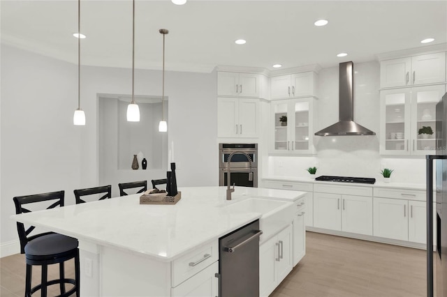 kitchen with wall chimney range hood, a kitchen bar, appliances with stainless steel finishes, and white cabinetry