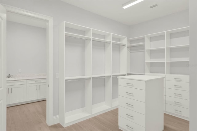 walk in closet with light wood-type flooring, a sink, and visible vents