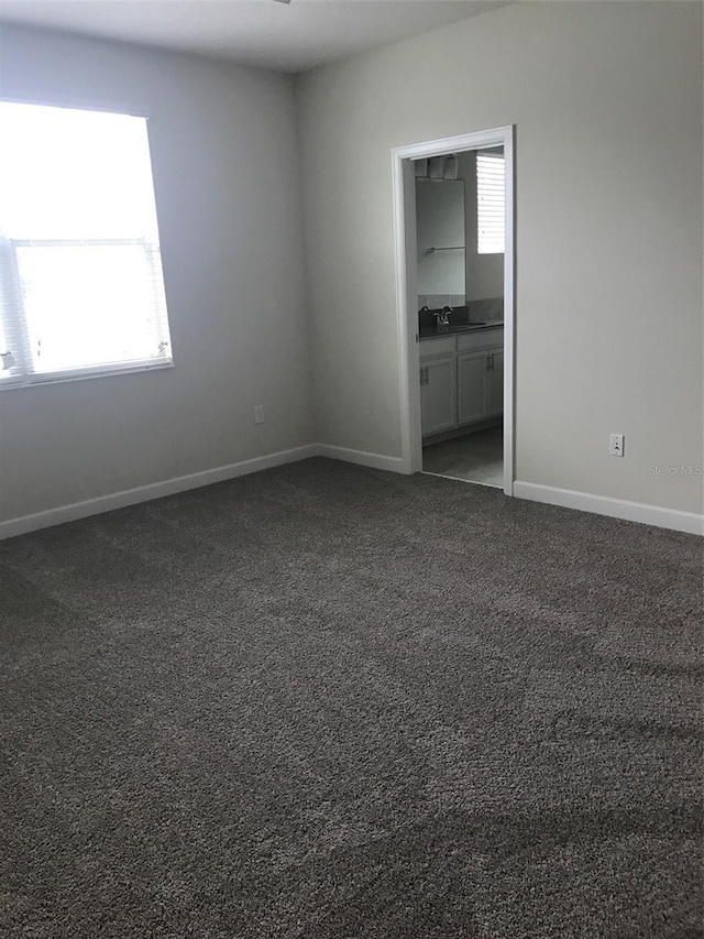 unfurnished bedroom with dark colored carpet, ensuite bathroom, and sink