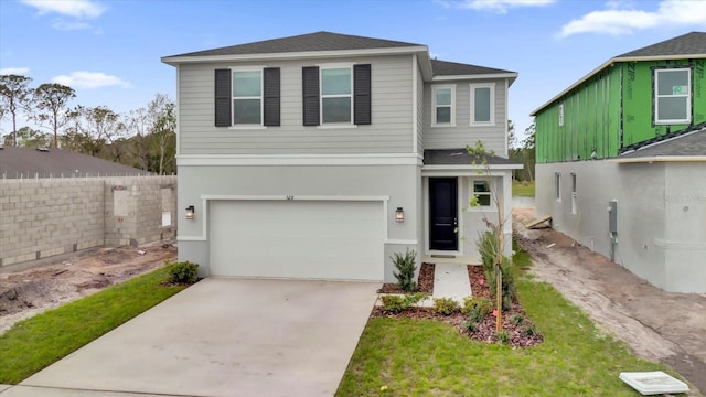 traditional home featuring driveway, an attached garage, fence, and stucco siding