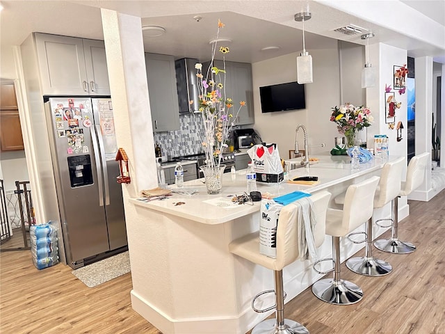 kitchen with a kitchen bar, light wood-type flooring, stainless steel appliances, gray cabinets, and hanging light fixtures