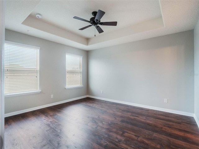 empty room with dark hardwood / wood-style floors, a raised ceiling, and ceiling fan