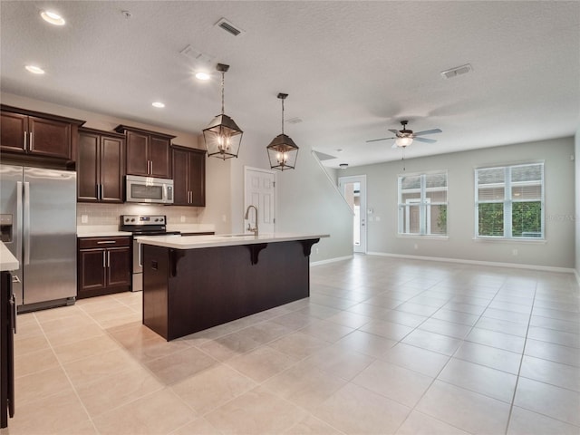 kitchen featuring appliances with stainless steel finishes, hanging light fixtures, a kitchen breakfast bar, tasteful backsplash, and a center island with sink