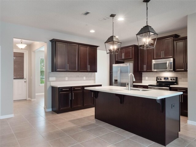 kitchen with sink, a breakfast bar area, hanging light fixtures, stainless steel appliances, and a center island with sink