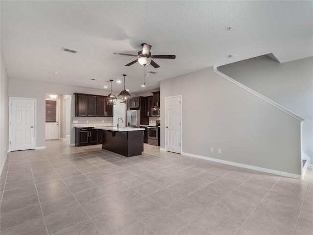 kitchen featuring pendant lighting, ceiling fan, appliances with stainless steel finishes, a center island with sink, and light tile patterned flooring