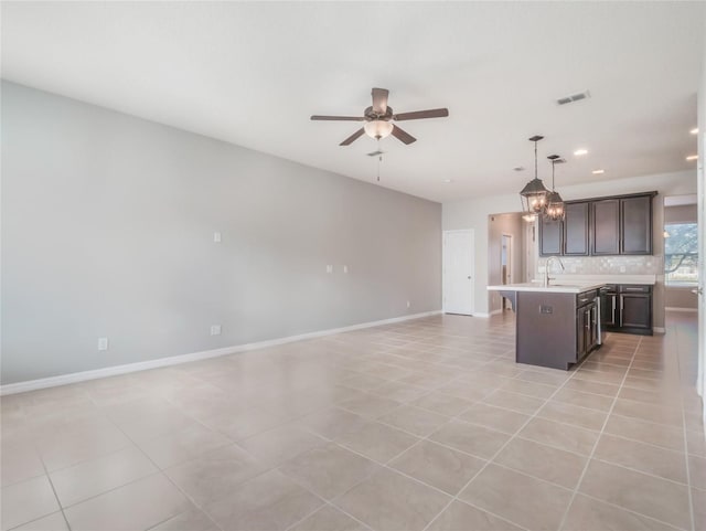 kitchen with dark brown cabinetry, decorative light fixtures, light tile patterned floors, an island with sink, and backsplash