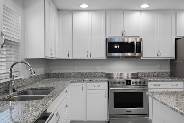 kitchen with appliances with stainless steel finishes, sink, light stone counters, and white cabinetry