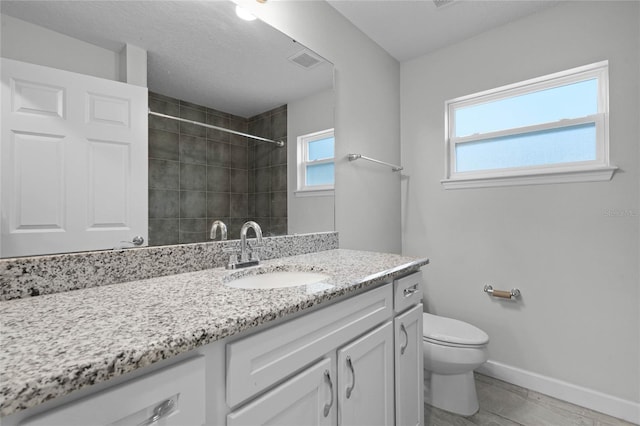 bathroom featuring toilet, vanity, plenty of natural light, and tiled shower