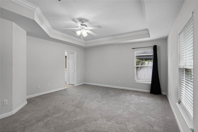 empty room with ceiling fan, a tray ceiling, a textured ceiling, ornamental molding, and light carpet