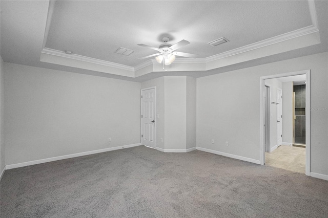 empty room with a raised ceiling, light colored carpet, ceiling fan, and crown molding