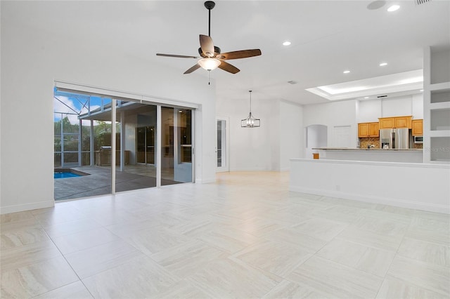 unfurnished living room featuring ceiling fan with notable chandelier, a raised ceiling, and light tile patterned floors