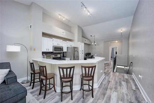 kitchen with stainless steel appliances, a kitchen breakfast bar, kitchen peninsula, pendant lighting, and white cabinets