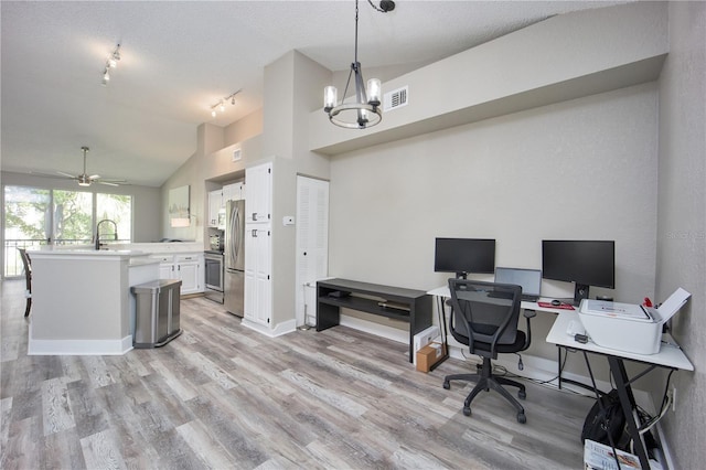 home office with ceiling fan with notable chandelier, rail lighting, vaulted ceiling, light wood-type flooring, and a textured ceiling