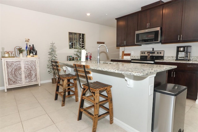 kitchen featuring a kitchen bar, a center island with sink, sink, appliances with stainless steel finishes, and light stone counters