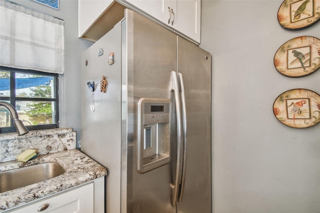 kitchen featuring stainless steel fridge, light stone counters, white cabinetry, and sink