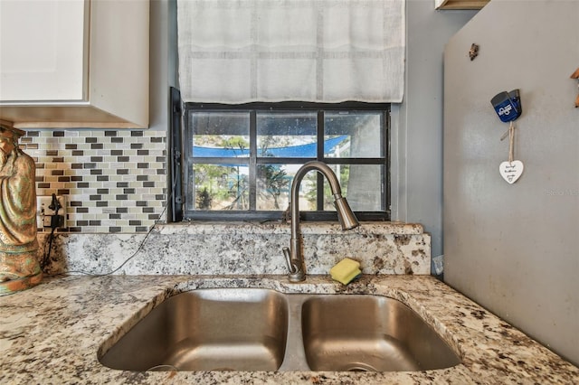 details with white cabinets, decorative backsplash, light stone counters, and sink