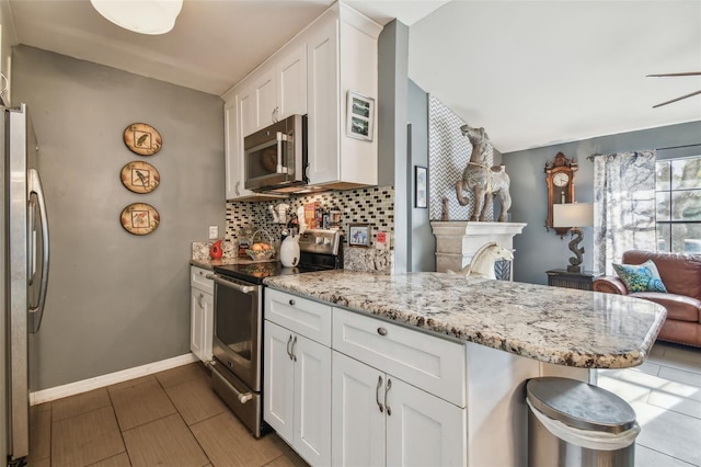 kitchen featuring stainless steel appliances, a peninsula, white cabinetry, decorative backsplash, and light stone countertops