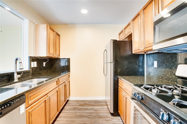 kitchen with appliances with stainless steel finishes, tasteful backsplash, sink, light hardwood / wood-style flooring, and dark stone countertops