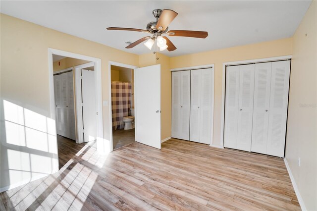 unfurnished bedroom with two closets, light hardwood / wood-style floors, ensuite bath, and ceiling fan