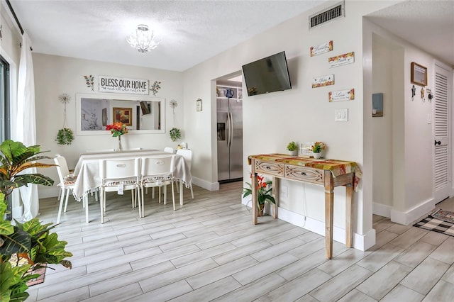 dining space featuring a notable chandelier, light hardwood / wood-style floors, and a textured ceiling