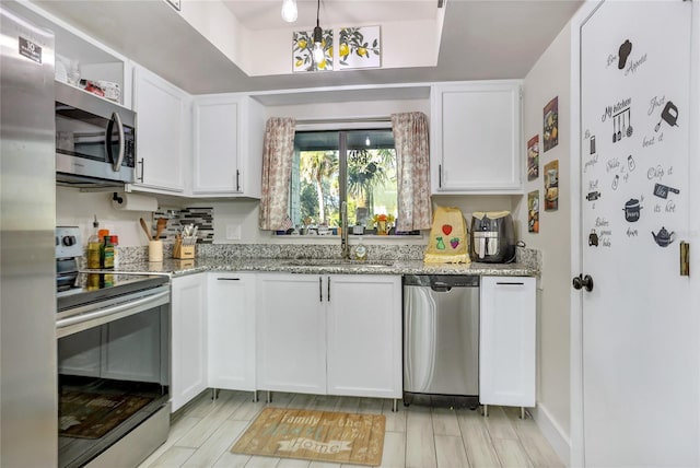 kitchen with white cabinetry, sink, light stone countertops, an inviting chandelier, and appliances with stainless steel finishes