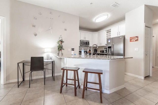 kitchen featuring kitchen peninsula, light stone countertops, appliances with stainless steel finishes, a kitchen breakfast bar, and white cabinets