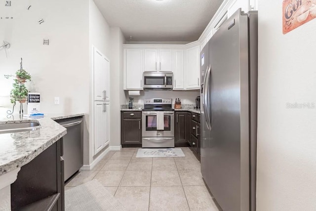 kitchen featuring sink, light tile patterned floors, light stone countertops, appliances with stainless steel finishes, and white cabinets