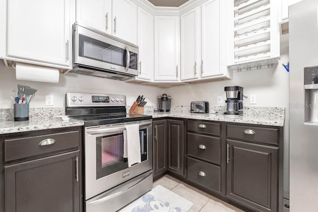 kitchen with light stone countertops, appliances with stainless steel finishes, dark brown cabinetry, white cabinetry, and light tile patterned floors