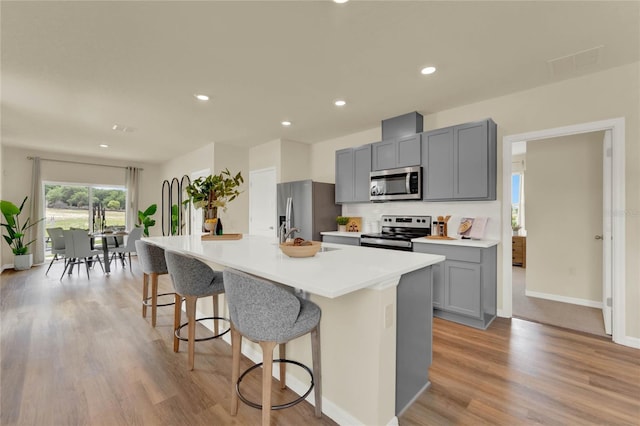 kitchen with a breakfast bar, a center island with sink, gray cabinets, light wood-type flooring, and stainless steel appliances