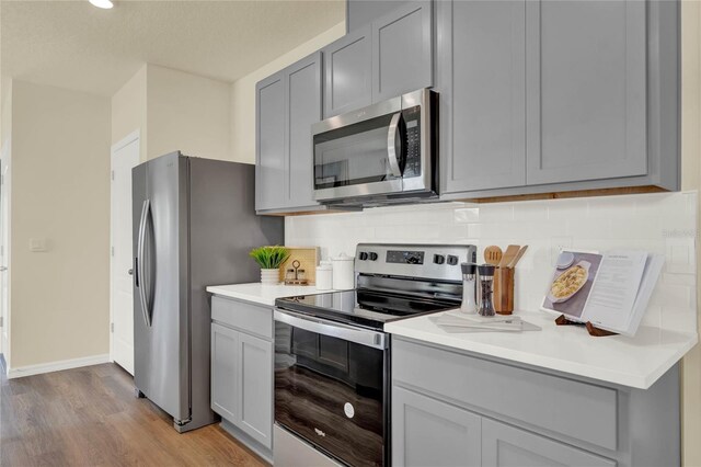 kitchen featuring gray cabinetry, decorative backsplash, light hardwood / wood-style flooring, and appliances with stainless steel finishes