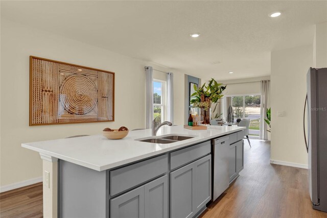 kitchen with appliances with stainless steel finishes, gray cabinetry, sink, light hardwood / wood-style flooring, and an island with sink