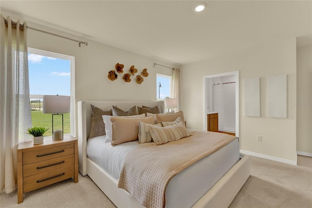 bedroom with light carpet, ensuite bathroom, and multiple windows