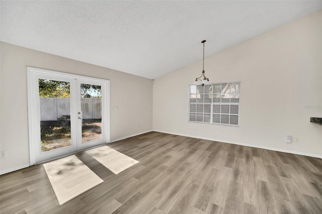 unfurnished dining area with wood-type flooring, lofted ceiling, a textured ceiling, and french doors