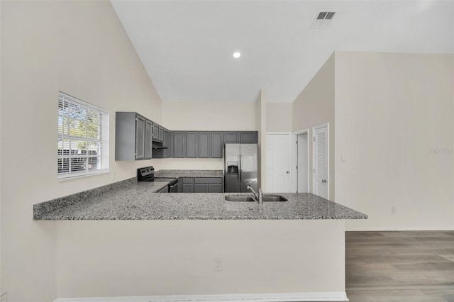 kitchen with sink, light stone counters, black / electric stove, stainless steel fridge, and kitchen peninsula