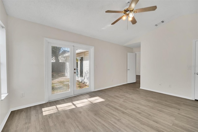 empty room with hardwood / wood-style floors, french doors, vaulted ceiling, ceiling fan, and a textured ceiling