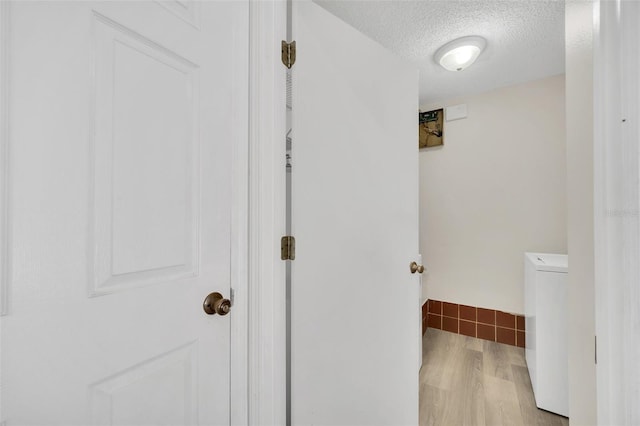 hall featuring washer / clothes dryer, light hardwood / wood-style flooring, and a textured ceiling