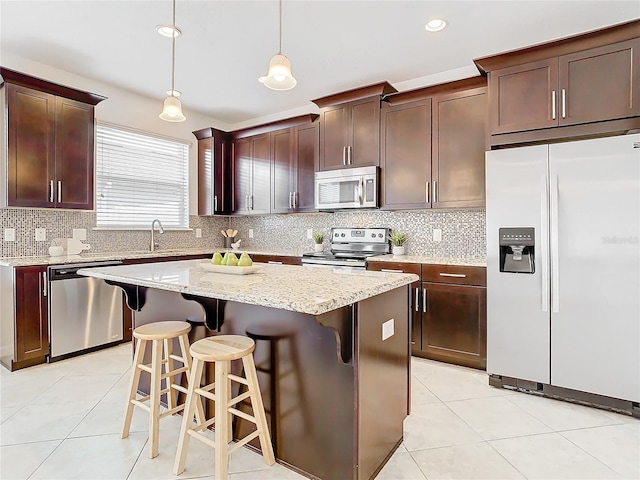 kitchen featuring sink, hanging light fixtures, stainless steel appliances, a center island, and a kitchen bar