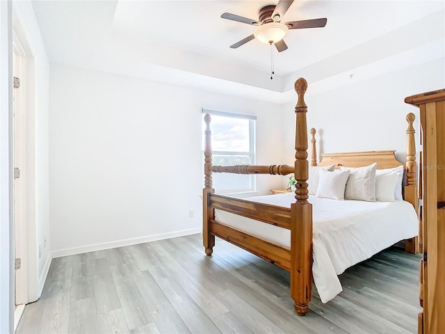 unfurnished bedroom with a raised ceiling, light wood-type flooring, and ceiling fan