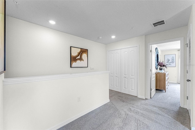 corridor featuring light carpet and a textured ceiling