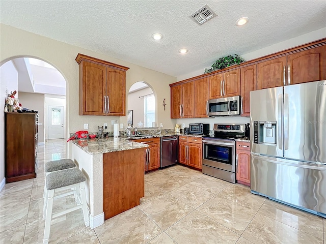 kitchen with kitchen peninsula, a textured ceiling, stainless steel appliances, and light stone counters